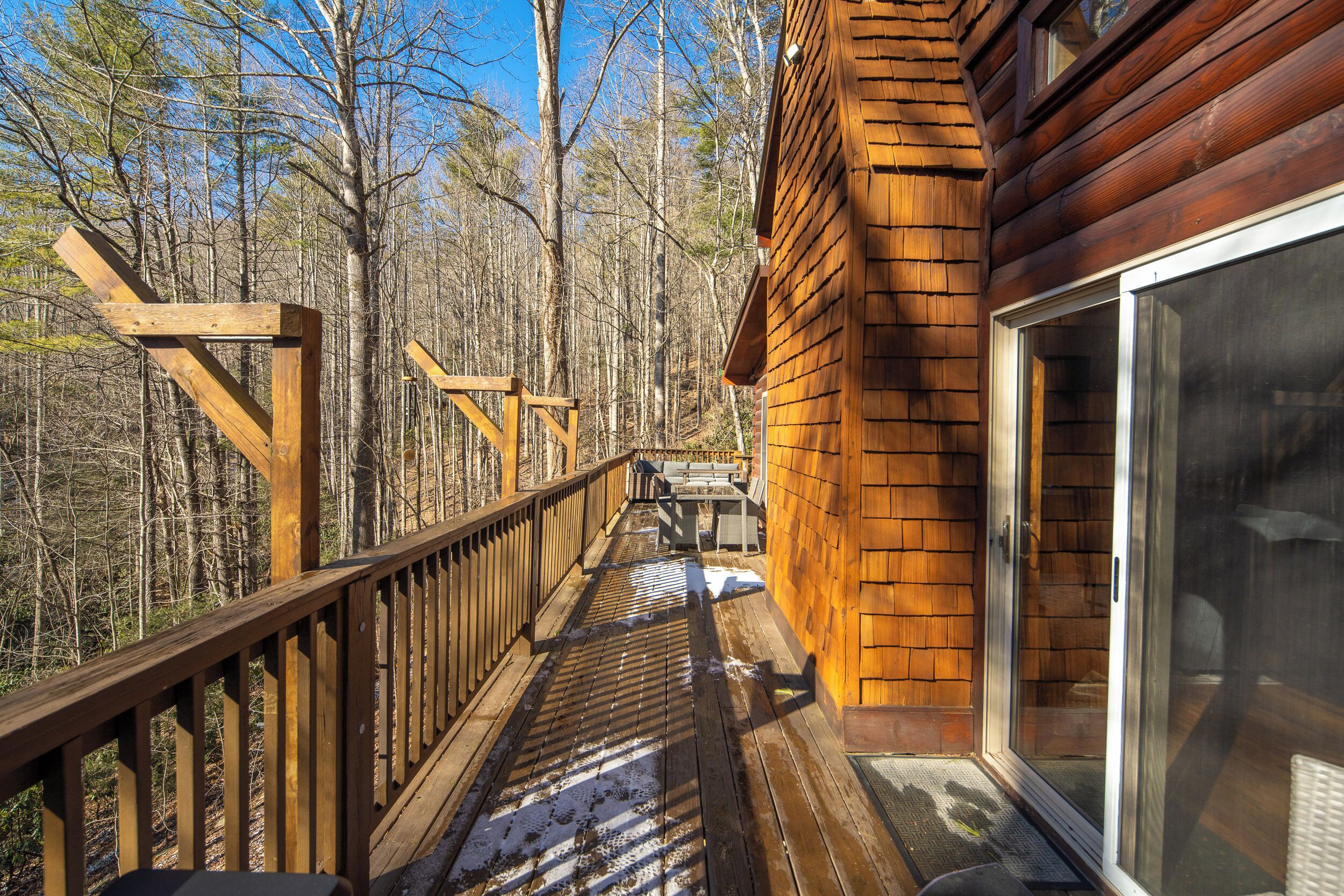 A wooden deck with a glass door leading to a covered outdoor area, surrounded by a forest.