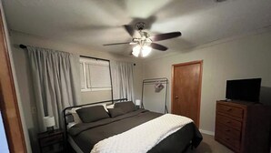 Un dormitorio con cama, ventilador de techo, cómoda y televisor.