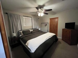 A bedroom with a bed, a ceiling fan, a dresser, and a television. - Cozy 4-bedroom 2-bath home near KSU Stadium (Manhattan)