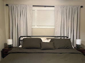 Una cama con estructura metálica, dos lámparas de noche y una ventana con persianas.
