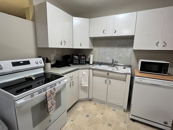 A kitchen with white cabinets, a stove, a microwave, and a dishwasher.