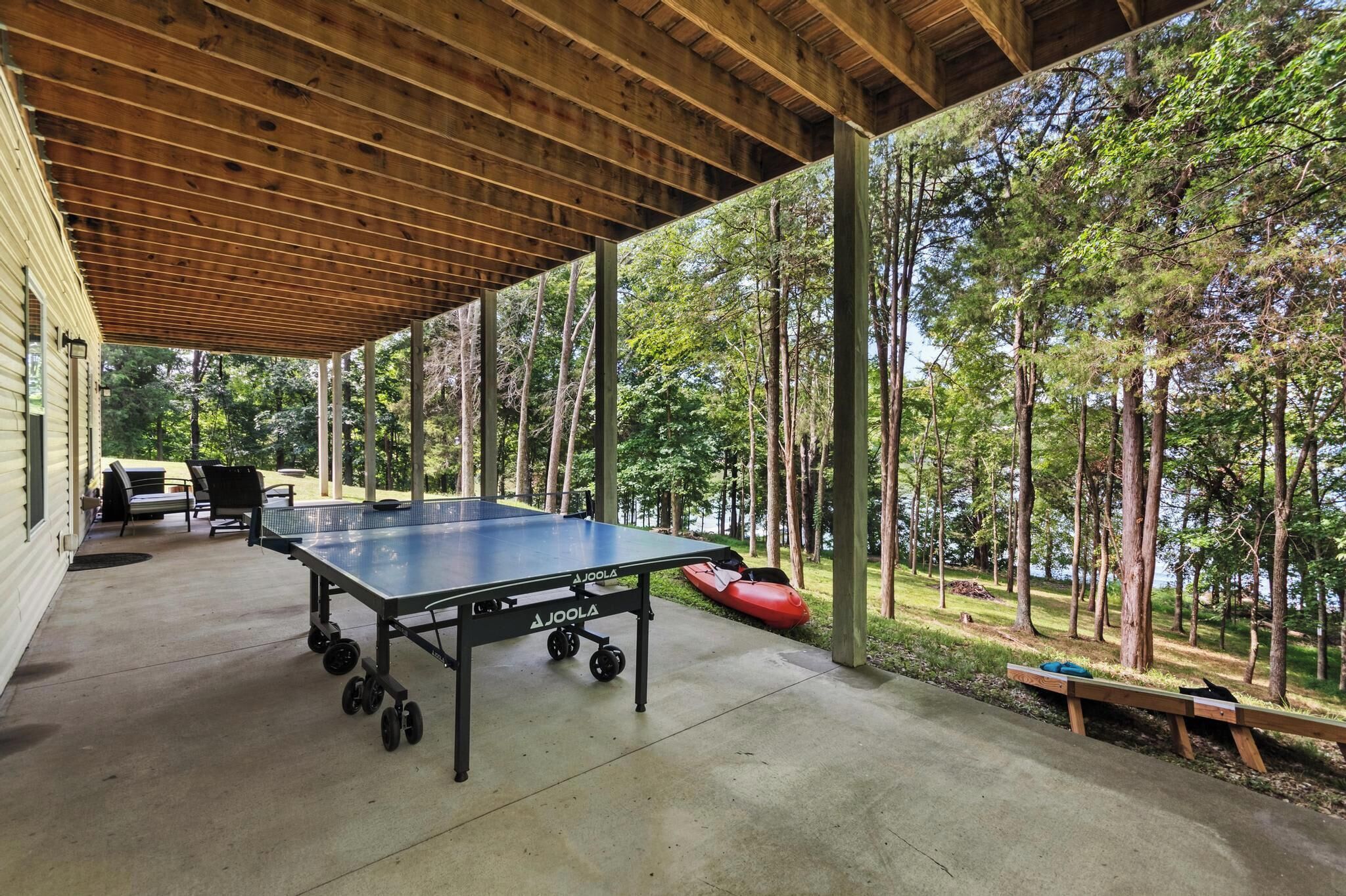 An outdoor table tennis table with wheels, a covered seating area, and a view of a forested area.
