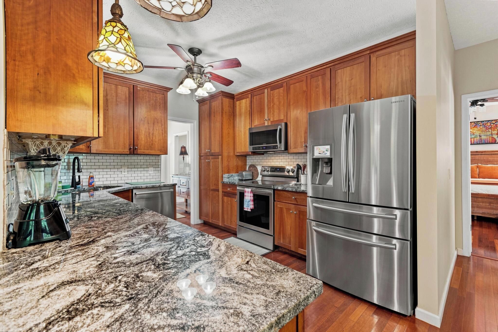 A kitchen with wooden cabinets, stainless steel appliances, a granite countertop, and a ceiling fan.