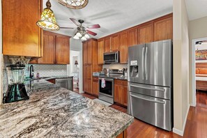 A kitchen with wooden cabinets, stainless steel appliances, a granite countertop, and a ceiling fan. - Shine Down Lakefront Retreat with Private Dock (Cadiz)