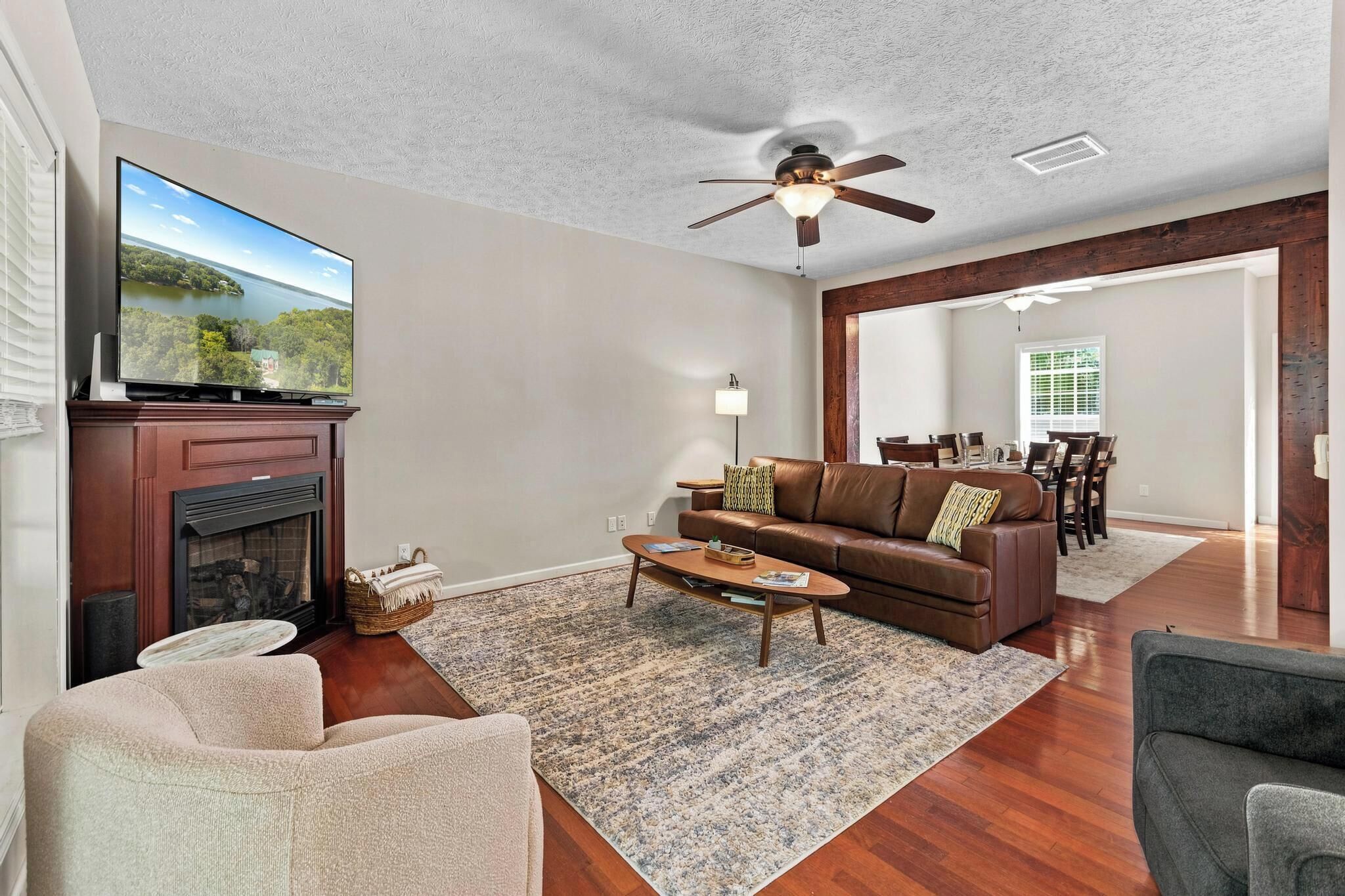 A living room with a fireplace, a television, a ceiling fan, and a dining area.