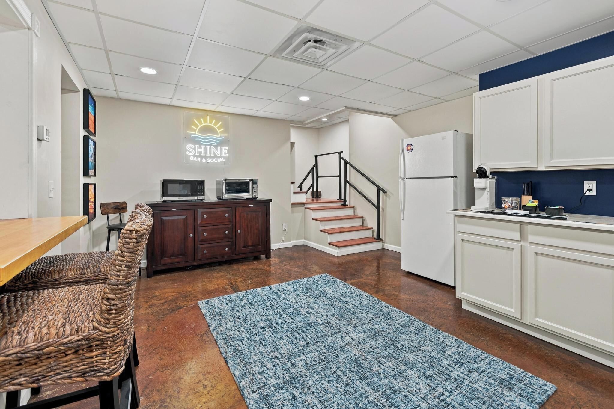 A kitchen with a microwave, toaster, and refrigerator, a dining area with a table and chairs, and a staircase leading to another level.