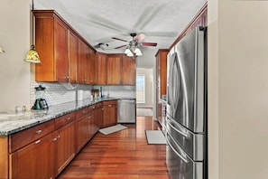 A kitchen with wooden cabinets, a stainless steel refrigerator, a ceiling fan, and a backsplash. - Shine Down Lakefront Retreat with Private Dock (Cadiz)