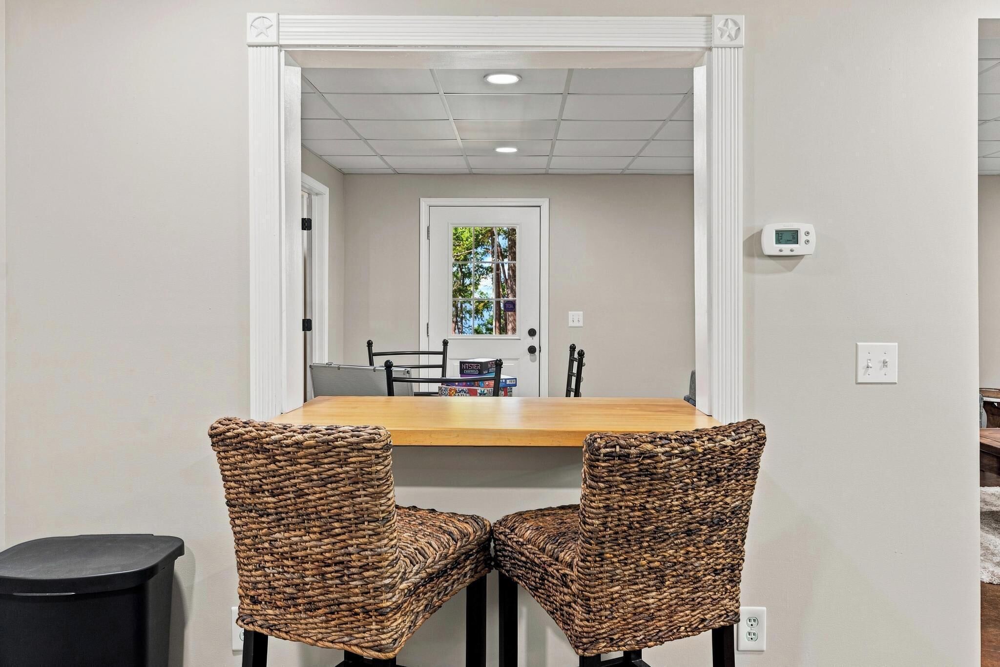 A dining area with a wooden table and two wicker chairs.