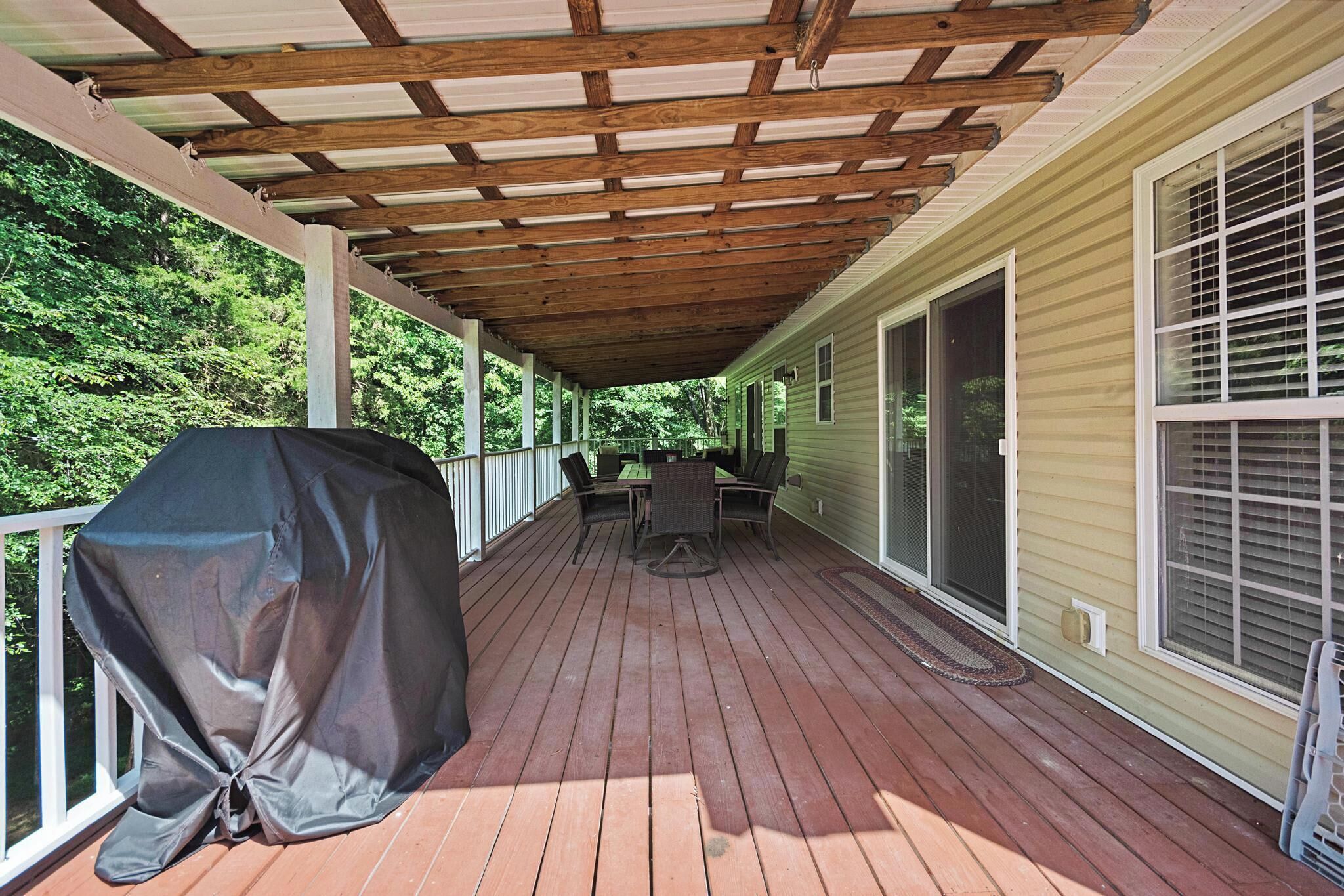 A covered deck with a grill, outdoor furniture, and a view of a house.