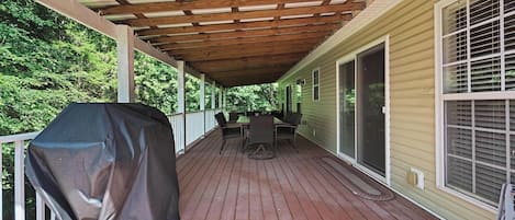 Una terraza techada con una parrilla, muebles de exterior y vistas a una casa.