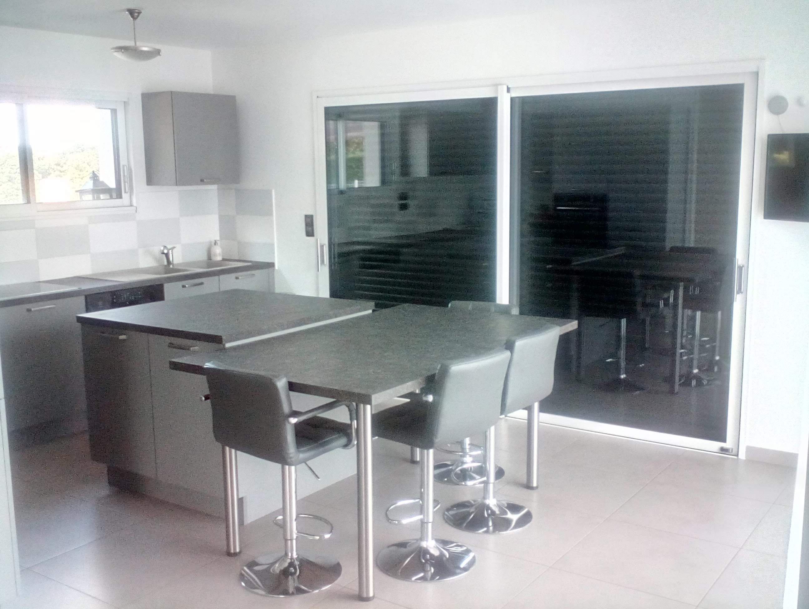 Una cocina moderna con una isla central, taburetes de bar y un puerta corrediza de vidrio que da a un comedor.