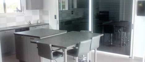 Una cocina moderna con una isla central, taburetes de bar y un puerta corrediza de vidrio que da a un comedor.