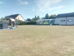 A grassy outdoor area with a playground, a building with a glass facade, and a clear sky. - Domaine d’architecte d'exception dans un ensemble moderne et sécurisé. (La Gravelle)