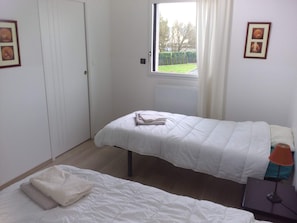 A bedroom with two beds, a window with curtains, a radiator, and framed pictures on the wall. - Domaine d’architecte d'exception dans un ensemble moderne et sécurisé. (La Gravelle)