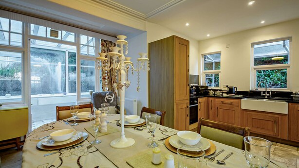 A dining room with a table set for a meal, a kitchen with modern appliances, and large windows providing natural light. - Host and Stay | BKL Seaview House (Colwyn Bay)