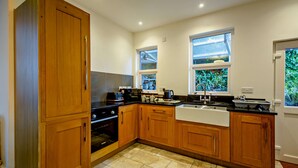 A kitchen with wooden cabinets, a black countertop, a built-in oven, a sink, and two windows with views of greenery. - Host and Stay | BKL Seaview House (Colwyn Bay)