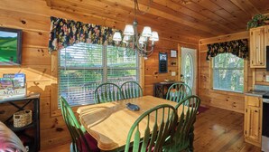 Interior em madeira com uma mesa de jantar, cadeiras, um lustre e vista pela janela.
