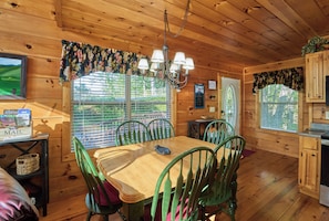A wooden interior with a dining table, chairs, a chandelier, and a view through the window. - Peaceful Cabin with Hot Tub, Game Room & Mtn Views (Sevierville)