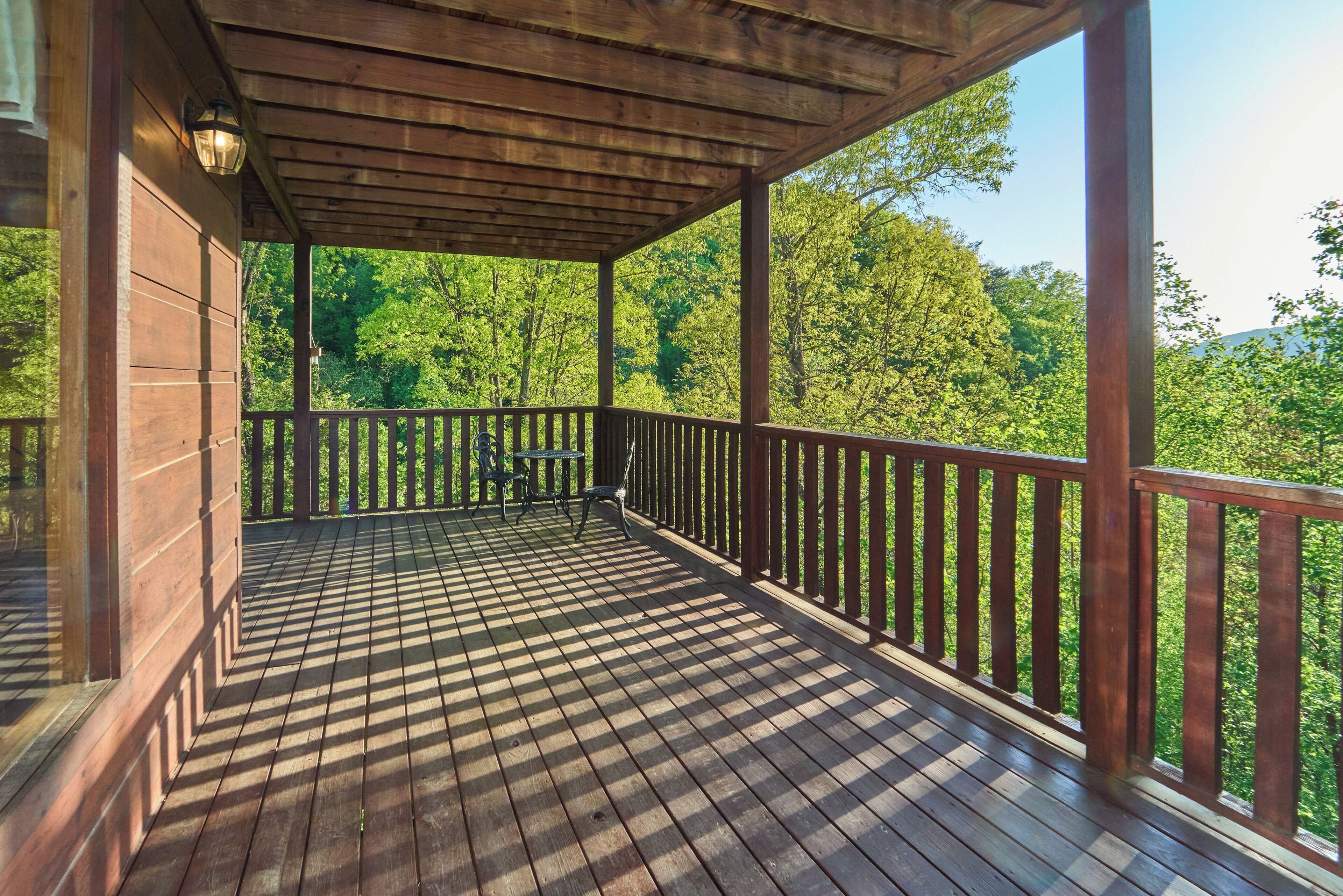 A wooden deck with a railing, a table, and chairs, overlooking a forested area.