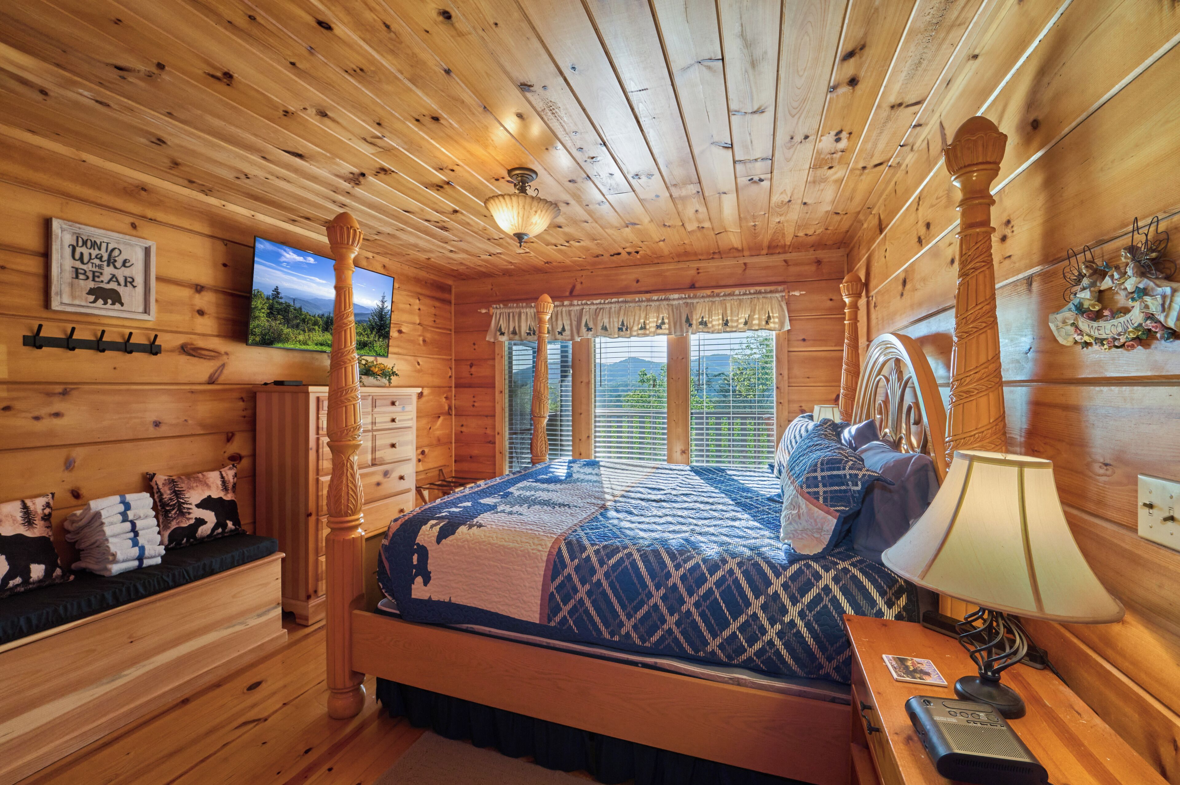 A wooden cabin bedroom with a bed, dresser, and a 'Welcome' sign.