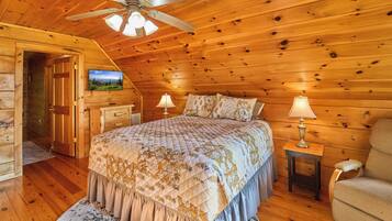 Une chambre à coucher aménagée dans un chalet en rondins, avec un lit, deux lampes de chevet, un ventilateur de plafond et un téléviseur fixé au mur.