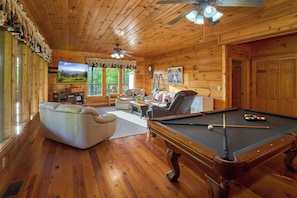 A wooden cabin interior with a pool table, a sofa, a television, and a fireplace. - Peaceful Cabin with Hot Tub, Game Room & Mtn Views (Sevierville)