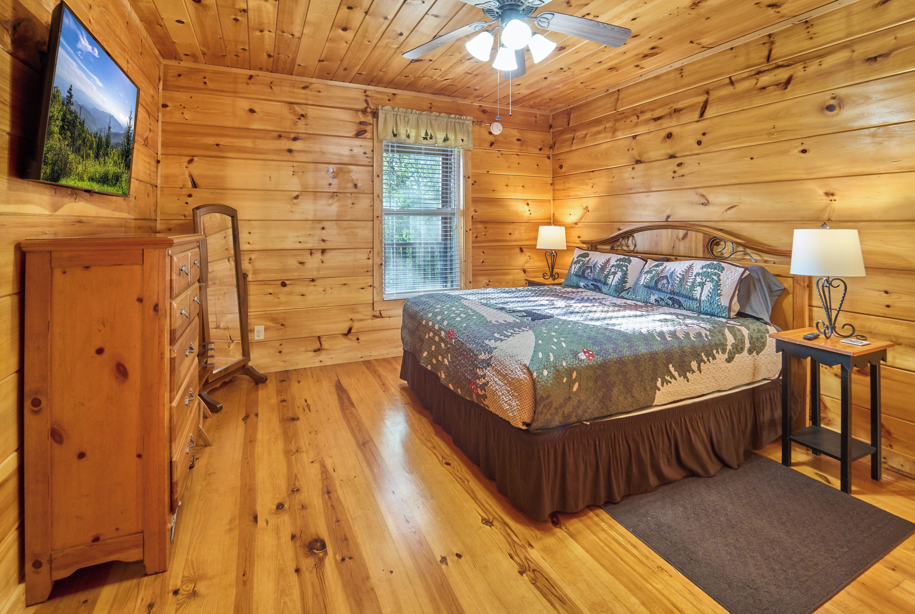 A wooden cabin bedroom with a bed, dresser, nightstands, and a ceiling fan.