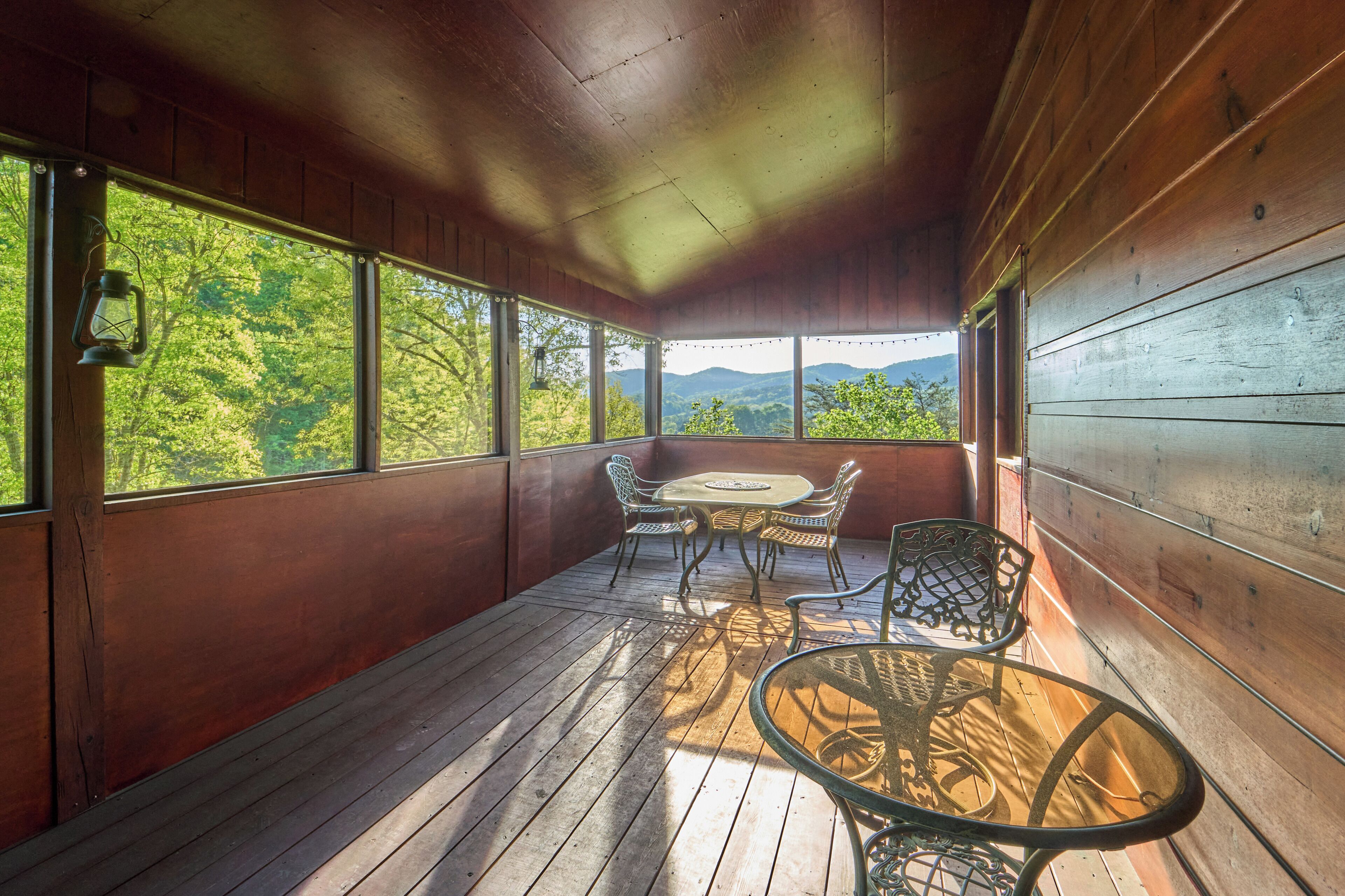 Une terrasse en bois avec une table et des chaises, de grandes fenêtres et une vue sur la verdure.