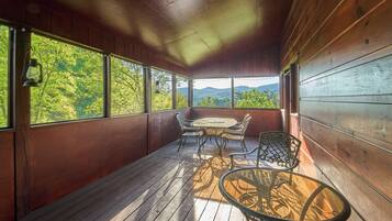 Une terrasse en bois avec une table et des chaises, de grandes fenêtres et une vue sur la verdure.