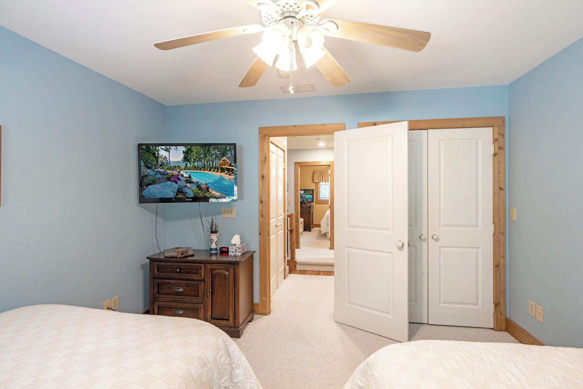 A bedroom with a bed, a dresser, a television mounted on the wall, and a ceiling fan.