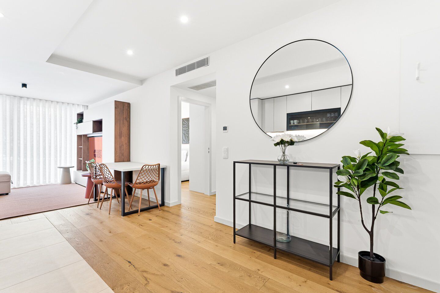 A modern living room with a dining area, a large mirror, and a potted plant.