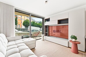 A modern hotel room with a large window, a sofa, a chair, a small table, and a wall-mounted TV displaying 'GUEST READY'. - GuestReady - Gaia Stay with Pool, Padel & Balcony (Vila Nova de Gaia)