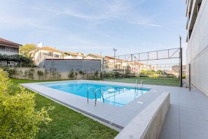 A rectangular swimming pool with a clear blue water surface, surrounded by a low white wall and a grassy area. - GuestReady - Gaia Stay with Pool, Padel & Balcony (Vila Nova de Gaia)