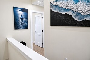 A hallway with a white door, a black trash bin, and two framed artworks on the wall. - Spectacular Waterfront Home - Coral Lagoon Unit #8 (Marathon)