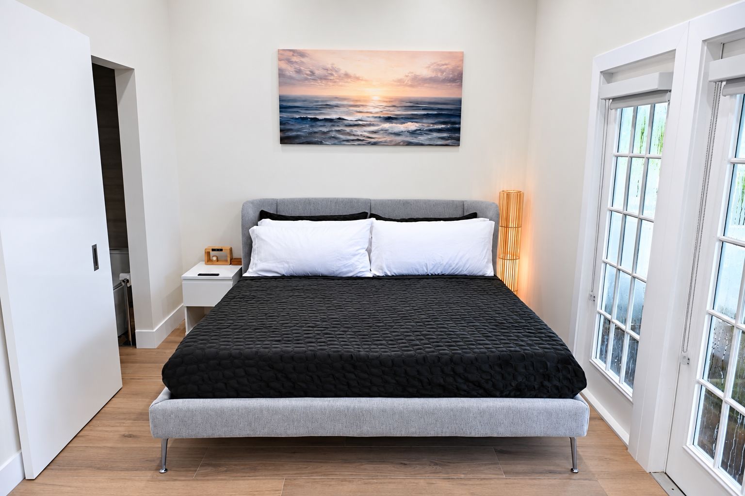 A modern bedroom with a bed, a nightstand, a wall-mounted painting, and a window with a view.