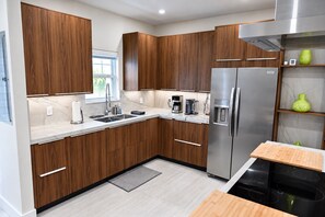 A modern kitchen with wooden cabinets, a stainless steel refrigerator, a built-in oven, and a coffee maker. - Spectacular Waterfront Home - Coral Lagoon Unit #8 (Marathon)
