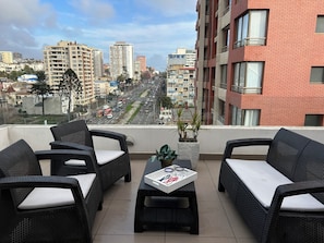 A balcony with wicker furniture, a small table with a laptop, and a view of a cityscape with buildings and a road. - The best terrace in downtown Viña del Mar (Viña del Mar)