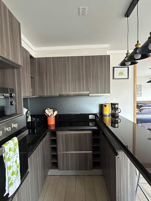 A compact kitchen with dark wood cabinets, a black countertop, and a small sink. There is a coffee maker and a basket of utensils on the counter. - The best terrace in downtown Viña del Mar (Viña del Mar)