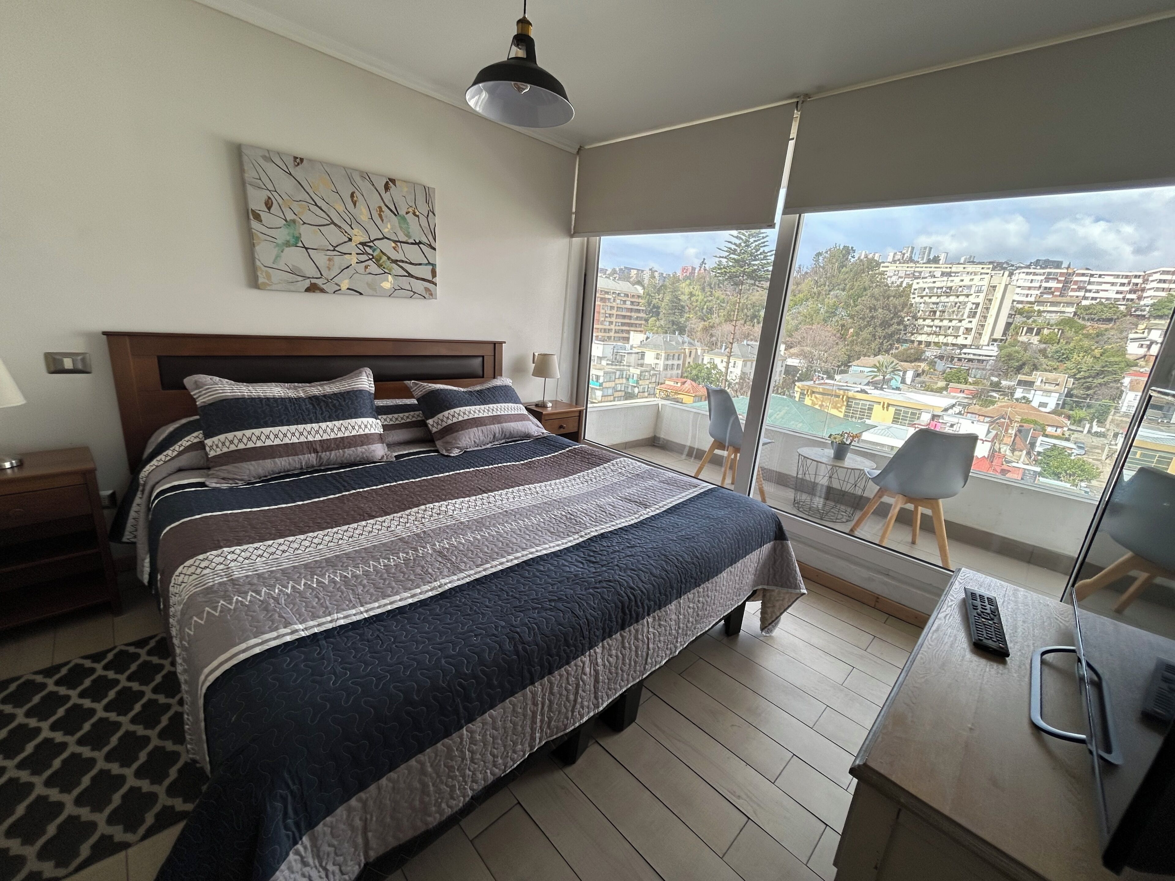 Ein modernes Schlafzimmer mit einem großen Bett, Stadtblick und einem Balkon mit einem Stuhl.