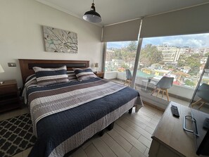 Een moderne slaapkamer met een groot bed, stadszicht en een balkon met een stoel.