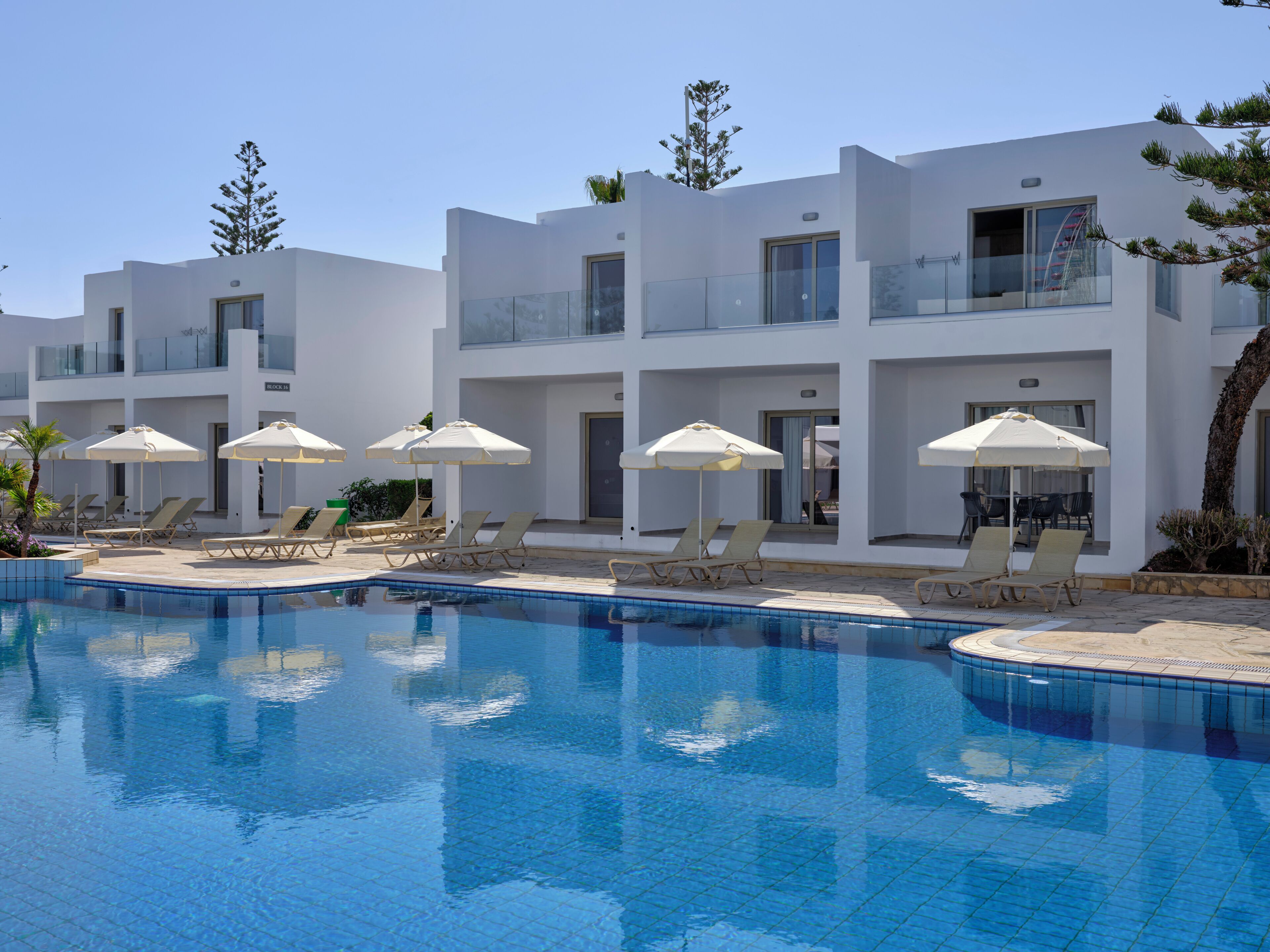 A modern hotel with a swimming pool, sun loungers, and umbrellas.