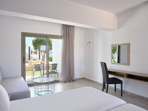 A modern hotel room with a large bed, a dining area with a table and chairs, a sliding glass door to an outdoor patio, and a mounted mirror on the wall. - Panthea Resort (Ayia Napa)