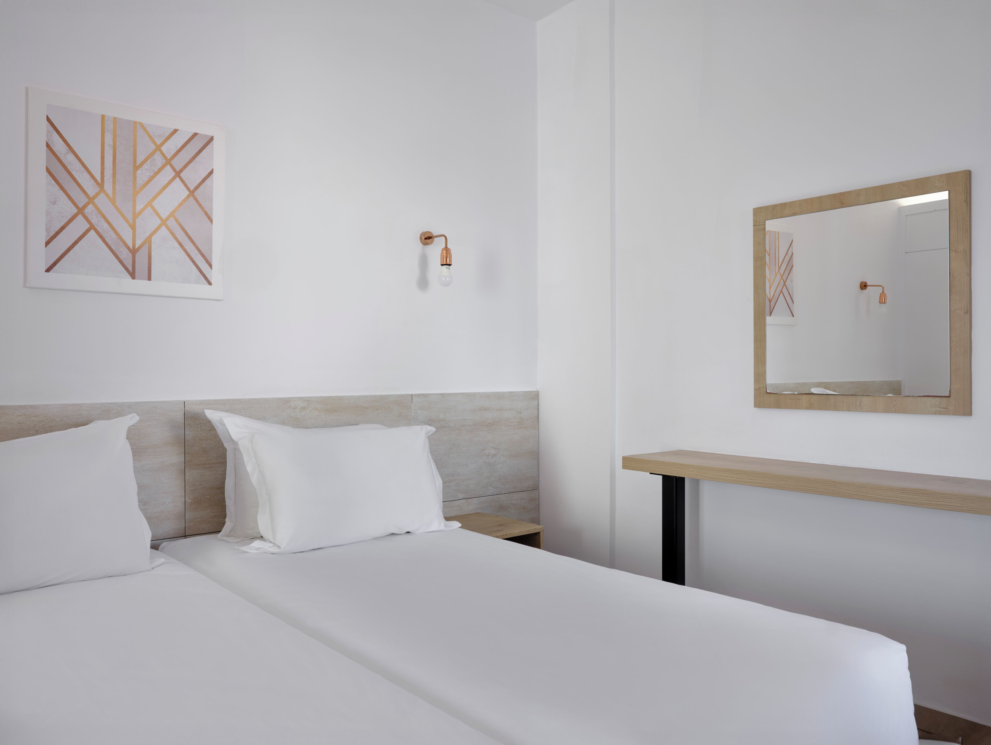 A hotel room with a bed, a bedside table, a wall-mounted mirror, and a wall art piece.