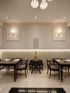 A dining area with two tables, chairs, wall-mounted lamps, a statue, and a recessed ceiling light. - Marvelous 6-bedroom bed & breakfast in the heart of Kandy (Kandy)