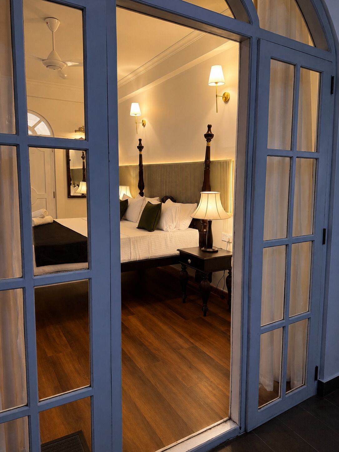 Une chambre d’hôtel avec un lit, une table de chevet, une lampe et un ventilateur de plafond.
