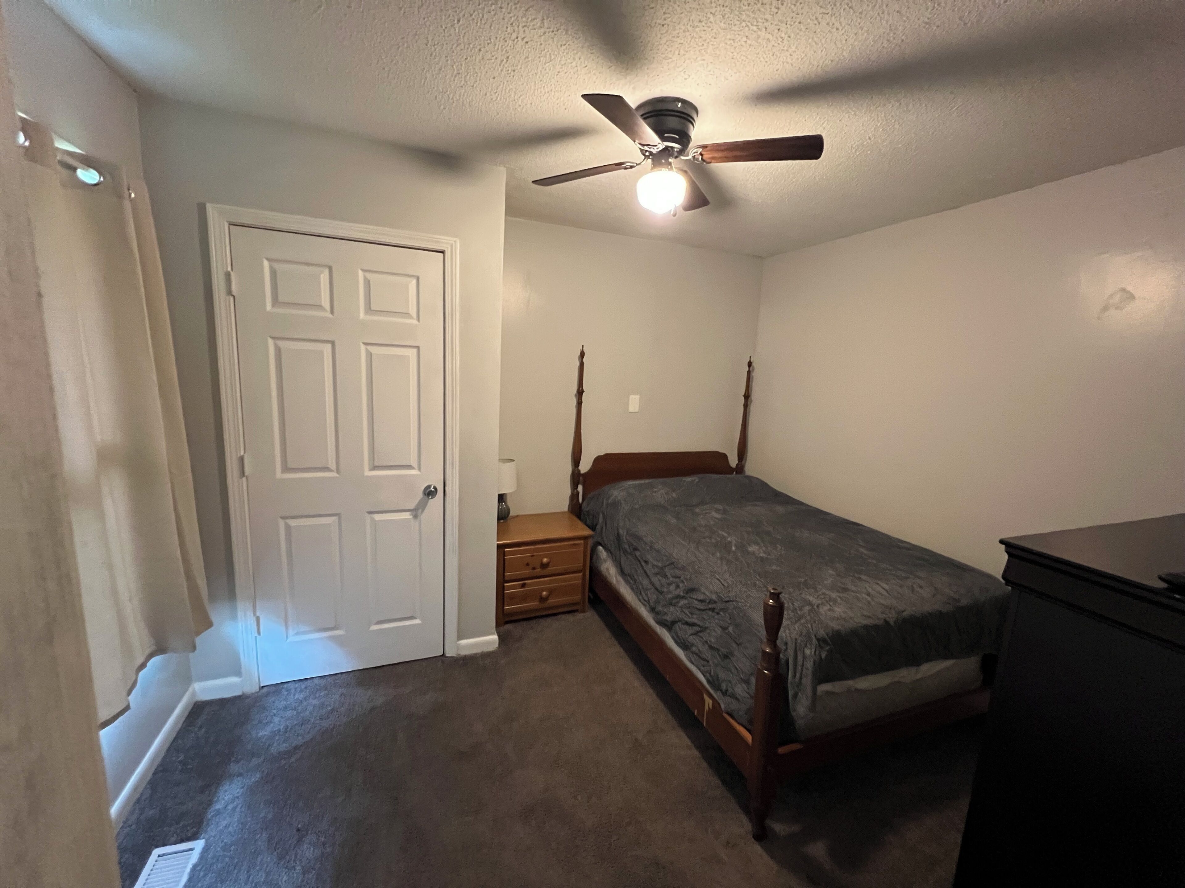 A bedroom with a single bed, a nightstand, a dresser, and a ceiling fan.