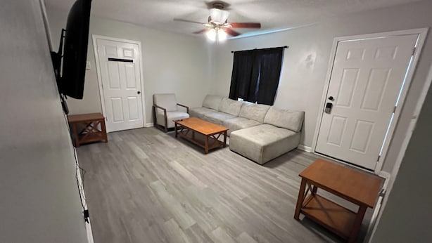 A living room with a sectional sofa, a coffee table, a TV mounted on the wall, and a ceiling fan. - Roomy 5BR Near I-95 & Fort Bragg - Family, Group & Work Stays (Fayetteville)