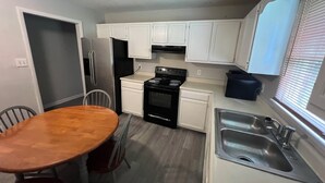 A compact kitchen with white cabinets, a black stove, a stainless steel sink, and a wooden dining table. - Roomy 5BR Near I-95 & Fort Bragg - Family, Group & Work Stays (Fayetteville)