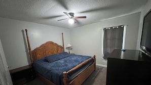 A bedroom with a wooden bed, a ceiling fan, a window with curtains, and a television on a stand. - Roomy 5BR Near I-95 & Fort Bragg - Family, Group & Work Stays (Fayetteville)