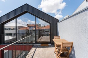 Un balcon moderne doté d’une paroi vitrée, d’une table et de chaises en bois, et offrant une vue sur des immeubles d’habitation.